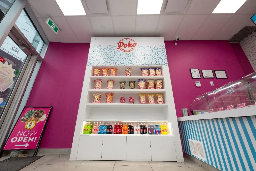 Product display shelves against a pink feature wall beside the service counter — POKO POPCORN — SURREY, BC