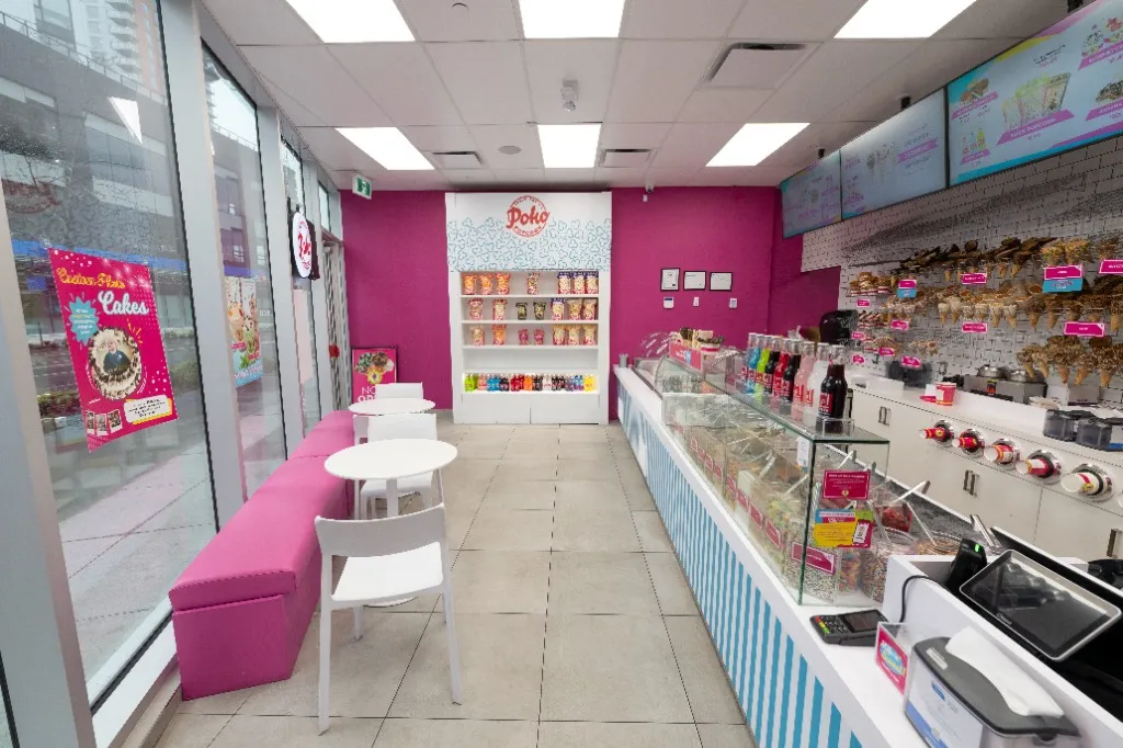 Pink upholstered bench and white tables opposite a glass retail display counter — POKO POPCORN — SURREY, BC