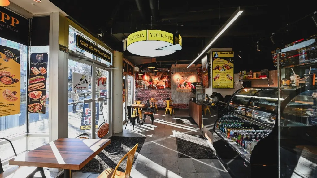Pizzeria display counter beside window seating and a circular ceiling sign — NONNA'S PIZZA — SURREY, BC