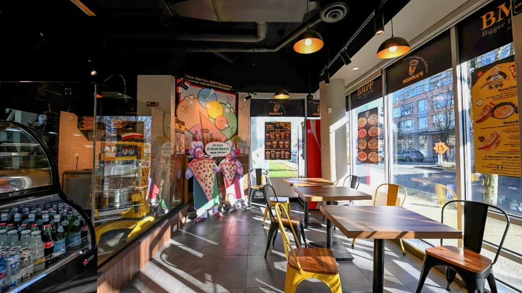 Pizzeria interior with a glass display counter and window-side dining tables — NONNA'S PIZZA — SURREY, BC